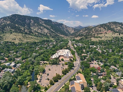Aerial view of the city of Boulder nestled against the foothills of the Rocky Mountains featuring lush green trees a winding road and residential buildings in Boulder Colorado United States. Aerial view of the city of Boulder nestled against the foothills of the Rocky Mountains featuring lush green trees a winding road and residential buildings in Boulder Colorado United States.