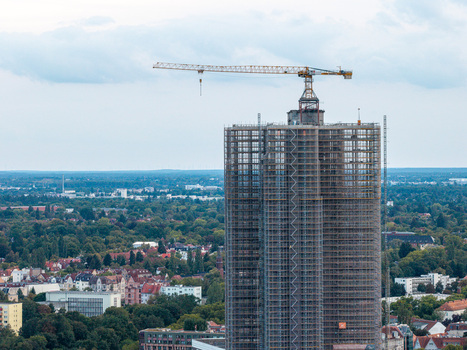 Aerial view of Steglitzer Kreisel skyscraper under renovation covered in scaffolding with a construction crane on top overlooking the urban landscape of Berlin Berlin Germany. Aerial view of Steglitzer Kreisel skyscraper under renovation covered in scaffolding with a construction crane on top overlooking the urban landscape of Berlin Berlin Germany.