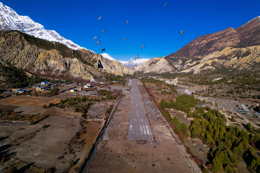 Aerial view of the airstrip in the Himalayas surrounded by snow capped peaks pine forests and rocky terrain under a clear blue sky in Nepal.