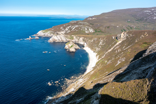 Aerial view of Glenlough Bay featuring rugged cliffs a secluded white sand beach and deep blue Atlantic waters in Ardara County Donegal Ireland.
