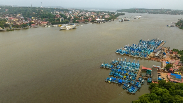 Aerial view of Atal Setu Goa bridge spanning the Mandovi River with a large fleet of blue fishing boats moored at the jetty in Panaji Goa India.