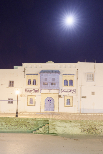 View of a traditional building with an ornate blue wooden balcony and arched doorway illuminated by a street lamp under a bright moon in Kairouan Kairouan Governorate Tunisia.