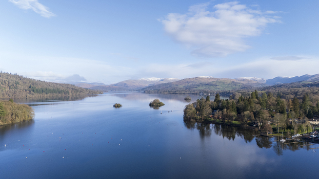 Aerial view of Windermere s tranquil waters reflecting the clear sky surrounded by lush green hills and the distant snow capped peaks Windermere England United Kingdom. Aerial view of Windermere s tranquil waters reflecting the clear sky surrounded by lush green hills and the distant snow capped peaks Windermere England United Kingdom.