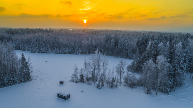 Aerial view of a snowy forest and frozen lake with small cabins at sunset in Latvia. Aerial view of a snowy forest and frozen lake with small cabins at sunset in Latvia.
