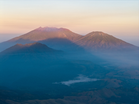 Aerial view of the Ijen volcano complex at sunrise with rugged mountain peaks soft morning light and mist settling in the valley below in Ijen East Java Indonesia.