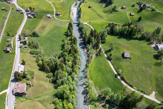 Aerial view of the Sarine river flowing through lush green meadows and traditional chalets in Rougemont Vaud Switzerland. Aerial view of the Sarine river flowing through lush green meadows and traditional chalets in Rougemont Vaud Switzerland.