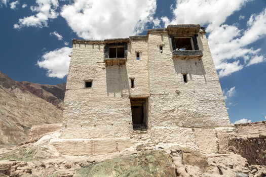View of the ancient white washed stone structure of Charasa Gonpa set against a rugged mountain landscape under a bright blue sky with scattered clouds in Charasa Ladakh India.