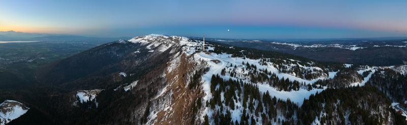 Aerial view of snow dusted peaks and verdant forests meet under a pastel sky crowned by a solitary tower Petit Mont Rond Auvergne Rh&ocirc;ne Alpes France.
