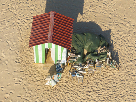 Figueira da Foz Portugal 08 August 2024 Aerial view of a striped beach hut on Praia da Figueira da Foz with stacked chairs and a person walking on the sand.