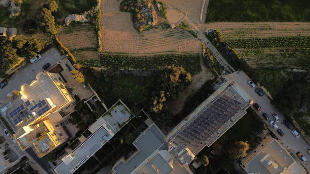 Aerial view of residential buildings with solar panels on rooftops adjacent to agricultural fields and a road with parked cars in Valletta Port Region Malta. Aerial view of residential buildings with solar panels on rooftops adjacent to agricultural fields and a road with parked cars in Valletta Port Region Malta.