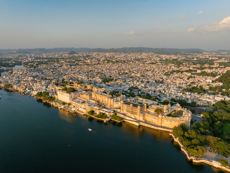 Aerial view of the City Palace complex on the banks of Lake Pichola with the historic city of Udaipur in the background in Udaipur Rajasthan India.