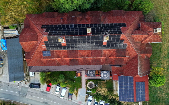 Aerial view of Brzece Sports Centar featuring a red tiled roof with solar panels surrounded by green trees a parking area and a road in Brzece Rasina District Serbia.