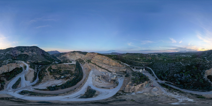 Aerial view of a large stone quarry with terraced rock faces and winding access roads surrounded by hills in Teulada Valencian Community Spain.