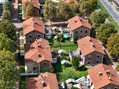 Aerial view of the historic brick houses and red tiled roofs of Villaggio Leumann surrounded by lush green gardens and trees in Collegno Piemonte Italy. Aerial view of the historic brick houses and red tiled roofs of Villaggio Leumann surrounded by lush green gardens and trees in Collegno Piemonte Italy.