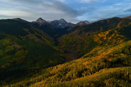Aerial view of Capitol Peak and the Elk Range in the Rocky Mountains featuring vibrant autumn fall foliage in the valley below at sunrise in Snowmass Colorado United States.