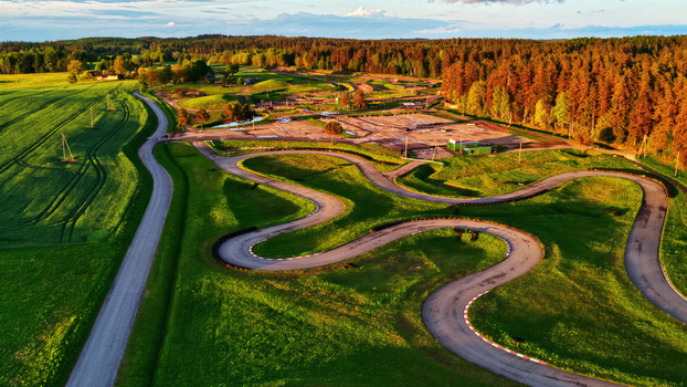 Aerial view of a winding go kart track surrounded by lush green grass and dense forest under the warm light of the golden hour in Latvia. Aerial view of a winding go kart track surrounded by lush green grass and dense forest under the warm light of the golden hour in Latvia.