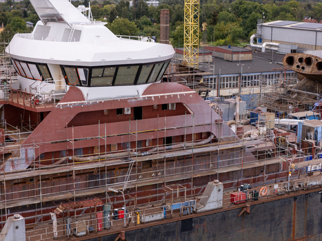 Aerial view of a ship under construction in a shipyard featuring a white bridge structure metal hull scaffolding and a yellow crane in the background in Gdansk Poland. Aerial view of a ship under construction in a shipyard featuring a white bridge structure metal hull scaffolding and a yellow crane in the background in Gdansk Poland.