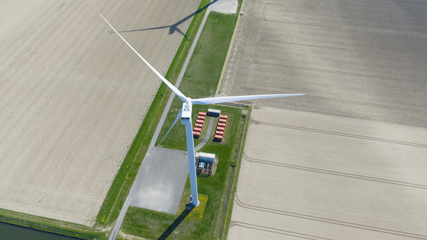 Aerial view of a large wind turbine at Energiepark Haringvliet Zuid with its shadow cast over agricultural fields and battery storage units in Middelharnis South Holland Netherlands.
