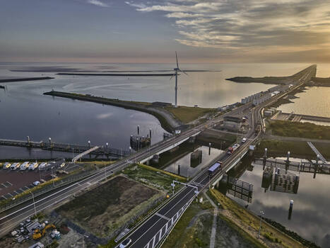 Den Oever Netherlands 19 June 2026 Aerial view of the Stevinsluizen sluice dams and A7 highway swing bridges with a wind turbine and the Waddenzee in early morning light. Den Oever Netherlands 19 June 2026 Aerial view of the Stevinsluizen sluice dams and A7 highway swing bridges with a wind turbine and the Waddenzee in early morning light.