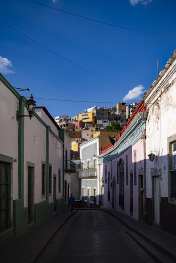 View of the historic narrow streets of Guanajuato Capital with colorful colonial buildings a person walking and hillside houses in Guanajuato Guanajuato Mexico. View of the historic narrow streets of Guanajuato Capital with colorful colonial buildings a person walking and hillside houses in Guanajuato Guanajuato Mexico.