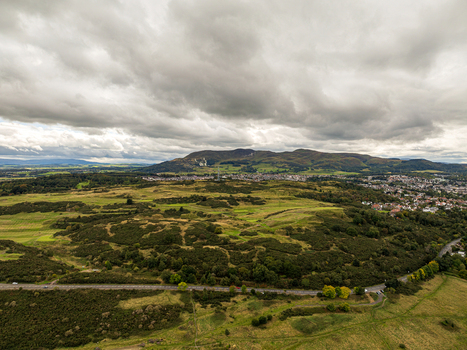 Aerial view of Braid Hills with rolling green terrain gorse covered slopes and distant urban outskirts under a cloudy sky in Edinburgh Scotland United Kingdom. Aerial view of Braid Hills with rolling green terrain gorse covered slopes and distant urban outskirts under a cloudy sky in Edinburgh Scotland United Kingdom.