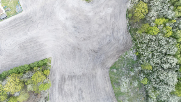 Aerial view of a tilled agricultural field with circular tire tracks bordered by lush green trees and spring vegetation Ourense Province of Ourense Spain. Aerial view of a tilled agricultural field with circular tire tracks bordered by lush green trees and spring vegetation Ourense Province of Ourense Spain.