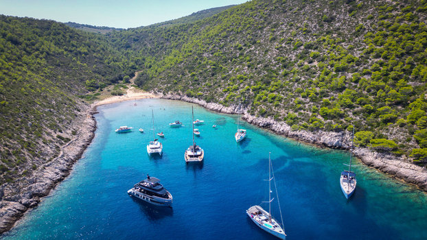 Aerial view of Smokova Bay with yachts and sailboats anchored in turquoise water surrounded by lush green hills in Vis Splitsko dalmatinska Croatia.