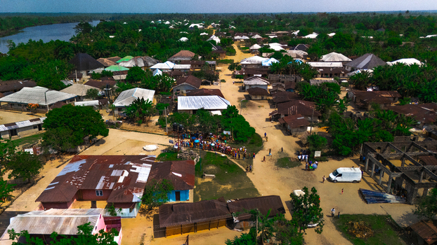 Aerial view of the village of Abua featuring traditional houses with metal roofs lush green vegetation a winding river and a dirt road in Abua Rivers Nigeria. Aerial view of the village of Abua featuring traditional houses with metal roofs lush green vegetation a winding river and a dirt road in Abua Rivers Nigeria.