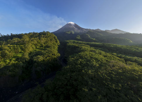 Aerial view of Mount Merapi volcano with smoke rising from the crater above the lush green forests of Bunker Kaliadem in Kecamatan Pakem Daerah Istimewa Yogya Indonesia. Aerial view of Mount Merapi volcano with smoke rising from the crater above the lush green forests of Bunker Kaliadem in Kecamatan Pakem Daerah Istimewa Yogya Indonesia.