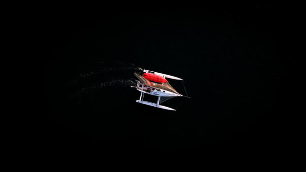 Aerial view of a lone sailboat cutting through the dark glassy waters its red accents a stark contrast against the deep abyss Plouezoc h Finistere France.