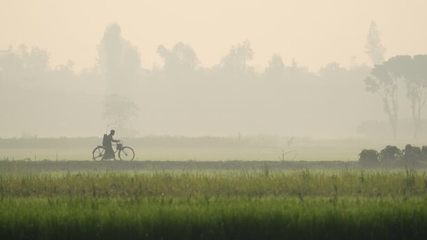 View of a man with a bicycle in a misty rural landscape Bangladesh.