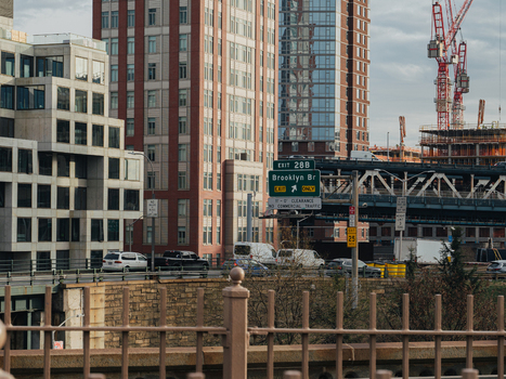View of the Brooklyn Bridge exit sign on a highway with urban skyscrapers and construction cranes in the background in New York New York United States.