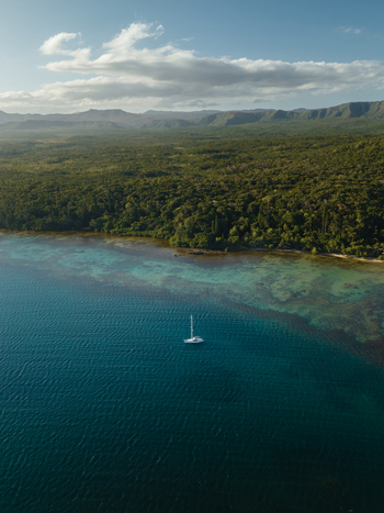 Aerial view of a lone sailboat gliding on the turquoise waters where the deep blue sea meets the lush green forest Goro South Province New Caledonia. Aerial view of a lone sailboat gliding on the turquoise waters where the deep blue sea meets the lush green forest Goro South Province New Caledonia.