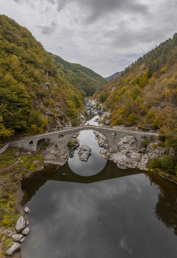 Aerial view of the historic stone Devil s Bridge arching over the Arda River surrounded by autumn colored forested hills and rocky banks in Kardzhali Province Bulgaria. Aerial view of the historic stone Devil s Bridge arching over the Arda River surrounded by autumn colored forested hills and rocky banks in Kardzhali Province Bulgaria.