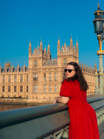 View of a woman in a striking red dress on a bridge admiring the iconic golden Parliament beneath a brilliant blue sky London England United Kingdom. View of a woman in a striking red dress on a bridge admiring the iconic golden Parliament beneath a brilliant blue sky London England United Kingdom.