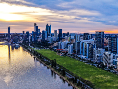 Aerial view of the Perth skyline at sunset with modern skyscrapers reflecting in the Swan River and lush green parkland along the waterfront in City of Perth Western Australia Australia.
