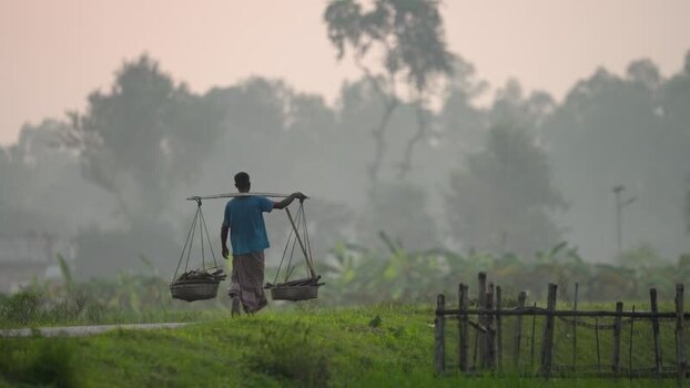 View of a man carrying baskets on a yoke in Bogura Bangladesh.