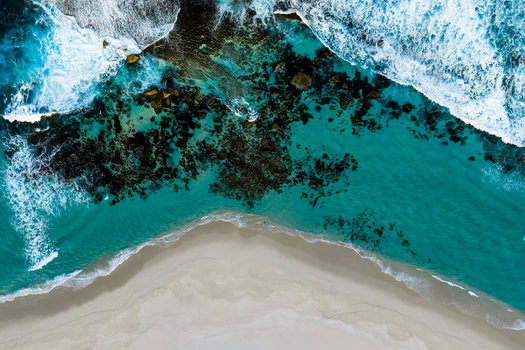 Aerial view of Salmon Holes with turquoise ocean waves crashing against dark rocky reefs and a pristine white sandy beach in Torndirrup Western Australia Australia.