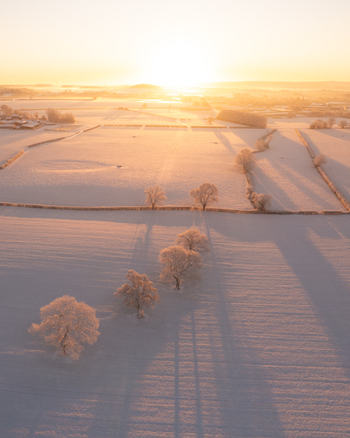 Aerial view of snow covered fields at sunrise with trees casting long shadows in Marston England United Kingdom. Aerial view of snow covered fields at sunrise with trees casting long shadows in Marston England United Kingdom.