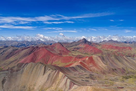 Aerial view of Vinicunca Rainbow Mountain with vibrant mineral rich striped slopes rugged Andean terrain and distant peaks under a clear blue sky. Cusco Cuzco Peru. Aerial view of Vinicunca Rainbow Mountain with vibrant mineral rich striped slopes rugged Andean terrain and distant peaks under a clear blue sky. Cusco Cuzco Peru.