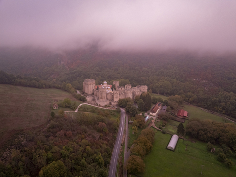 Aerial view of Manasija Monastery surrounded by lush green forests and misty hills with a road leading to the historic stone fortifications in Despotovac Pomoravski okrug Serbia.