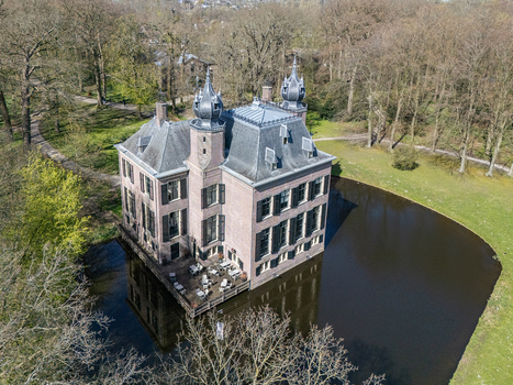 Aerial view of the historic Landgoed Oud Poelgeest castle a pinkish stone fortress mirrored in the dark waters surrounded by the verdant embrace of trees Oegstgeest Zuid Holland Netherlands. Aerial view of the historic Landgoed Oud Poelgeest castle a pinkish stone fortress mirrored in the dark waters surrounded by the verdant embrace of trees Oegstgeest Zuid Holland Netherlands.