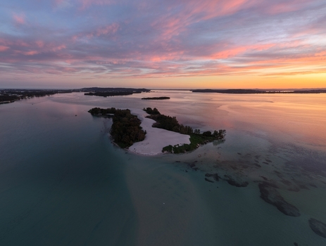 Aerial view of islands nestled in tranquil waters reflecting a pastel sky painted with hues of pink and gold Newcastle New South Wales Australia.