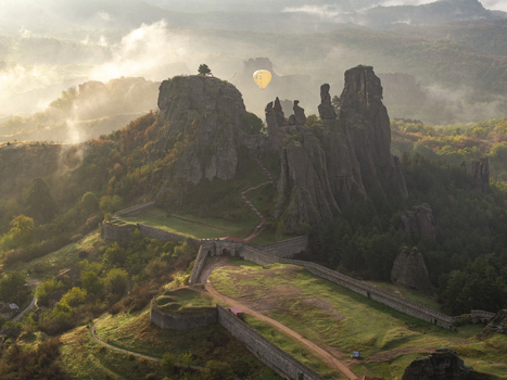 Aerial view of Belogradchik Fortress surrounded by dramatic sandstone rock formations and lush greenery in the morning mist with a hot air balloon Belogradchik Vidin Bulgaria. Aerial view of Belogradchik Fortress surrounded by dramatic sandstone rock formations and lush greenery in the morning mist with a hot air balloon Belogradchik Vidin Bulgaria.