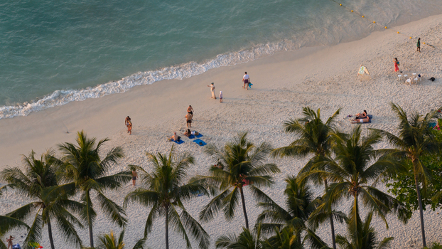 Aerial view of Freedom Beach with people relaxing on white sand under palm trees by turquoise water in Tambon Patong Chang Wat Phuket Thailand.