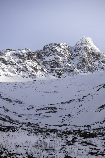 View of a majestic snow covered mountain peak with jagged ridges under a clear sky in Kvaloya Troms Norway. View of a majestic snow covered mountain peak with jagged ridges under a clear sky in Kvaloya Troms Norway.