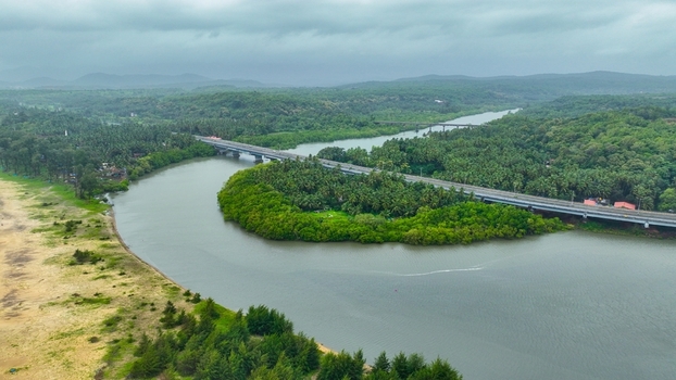 Aerial view of Galgibaga Beach with the Galgibaga River flowing through lush palm groves and crossed by a modern bridge in Canacona Goa India.