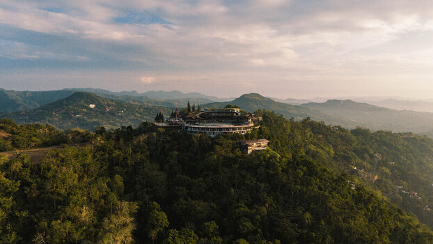 Cebu City Philippines 20 May 2026 Aerial view of the Busay area featuring a circular building perched on a lush green hilltop surrounded by tropical mountains under a soft sunset sky.