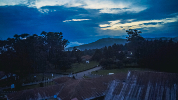 Aerial view of rustic rooftops and dark foliage contrast under a dramatic twilight sky with a majestic mountain range silhouetted against fading light Obudu Cross River Nigeria.