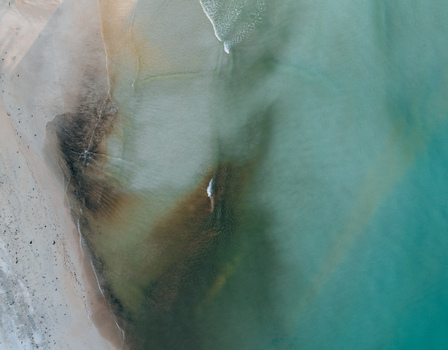 Aerial view of turquoise waters meet the sandy shore contrasting with dark patches beneath the surface Pantai Tanjung Aan West Nusa Tenggara Indonesia. Aerial view of turquoise waters meet the sandy shore contrasting with dark patches beneath the surface Pantai Tanjung Aan West Nusa Tenggara Indonesia.